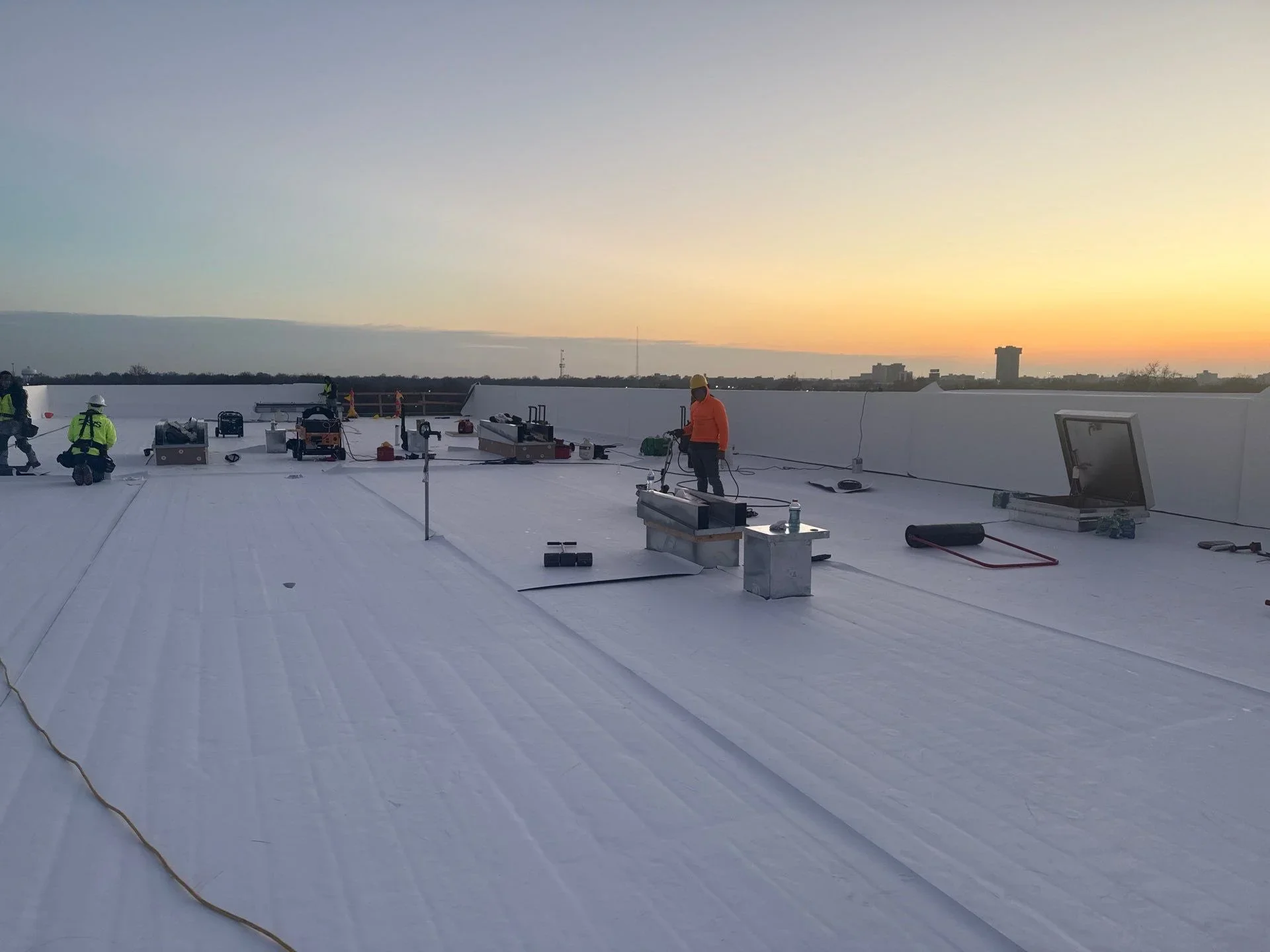 White TPO membrane flat roof installation with HVAC equipment and crew members on commercial building