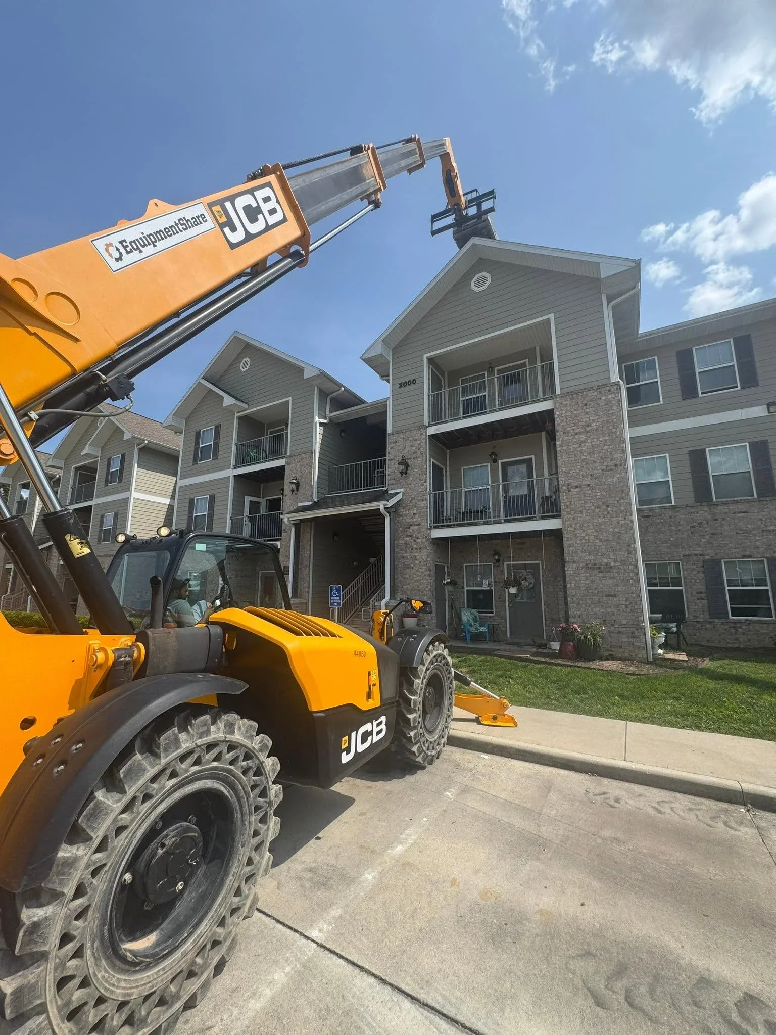 JCB telehandler crane lifting roofing materials to pitched roof of multi-story residential building