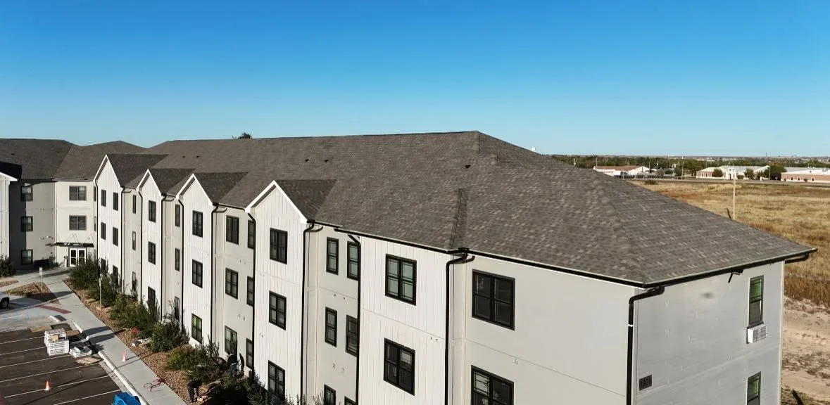 Charcoal gray architectural shingle roof on multi-unit residential building with white siding and gable peaks