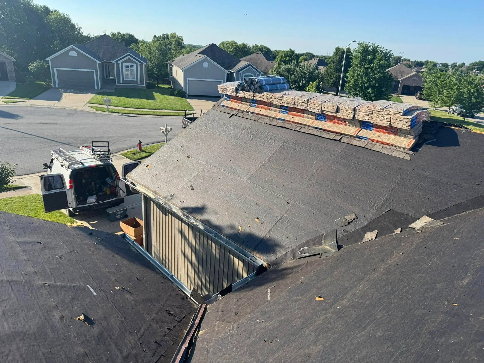 Roof stripped to decking with staged shingles, underlayment, and metal drip edge installation