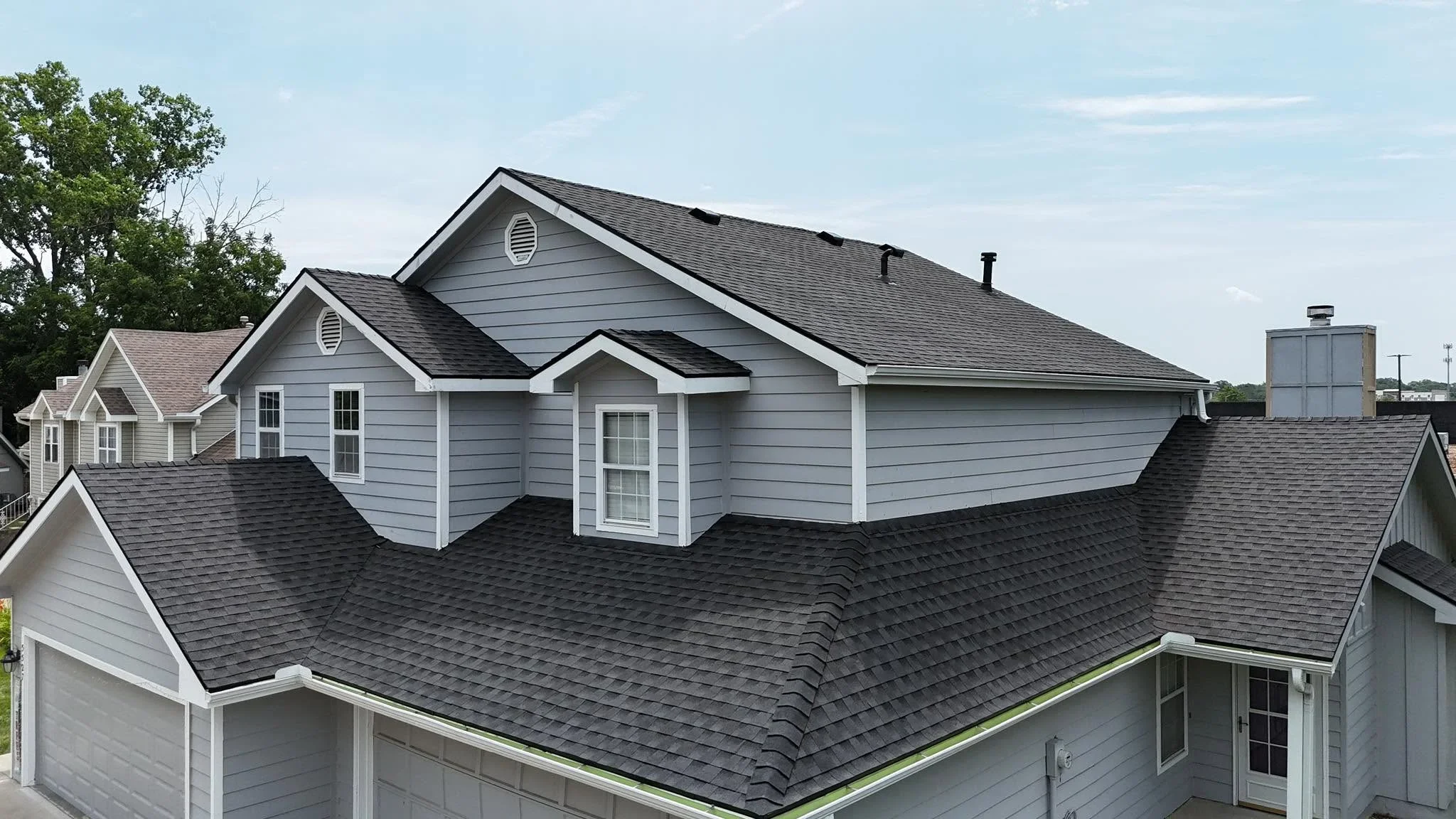 Charcoal gray architectural shingles on multi-pitch residential roof with dormers and white trim